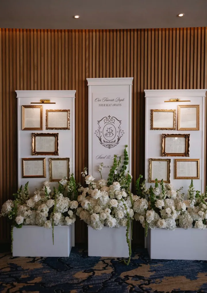 Seating chart wall with gold vintage frames and white florals