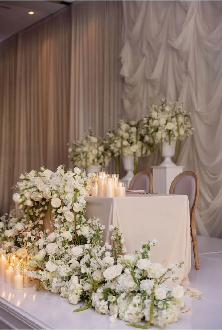 Sweetheart table on a white stage with candlelight and white roses